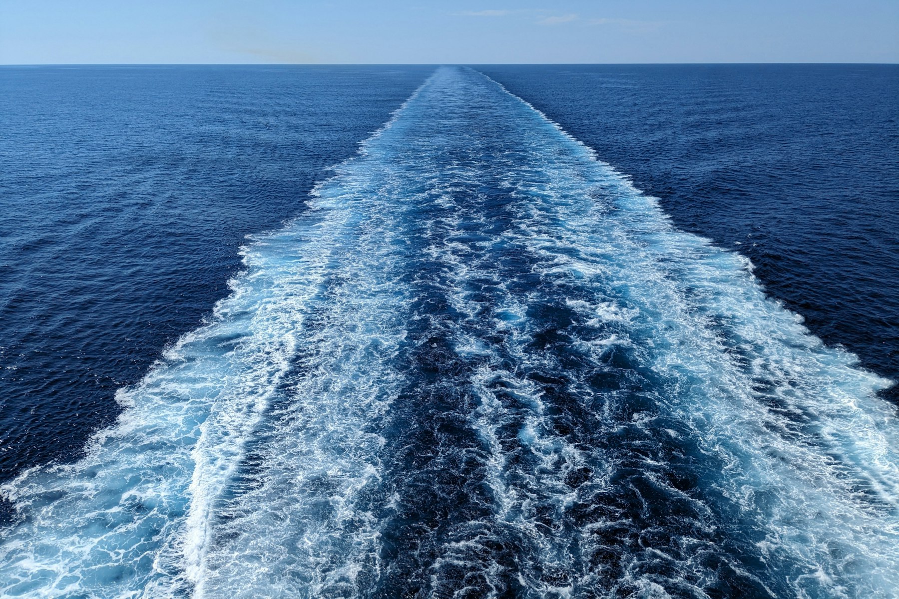 A ship's white wake stretching across a deep blue open sea to the horizon